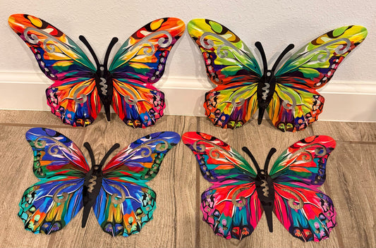 Four colorful butterfly wall art pieces arranged on a light wood floor against a white baseboard and wall.