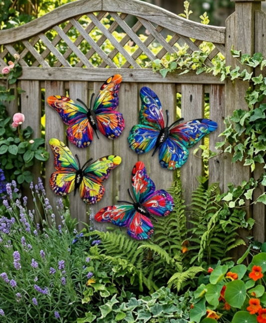 Four colorful metal butterfly garden decorations with vibrant painted wings, mounted on a wooden lattice fence in a lush garden setting with green plants and flowers.
